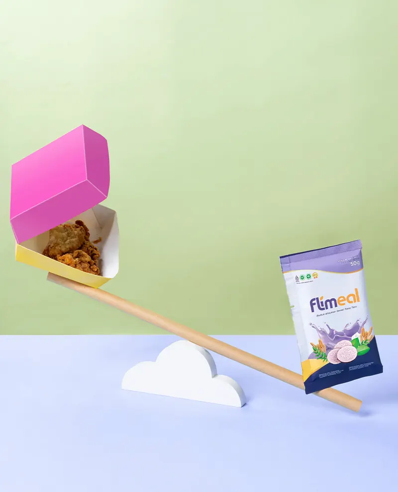Jungkat-jungkit dengan kotak ayam goreng di satu sisi dan sachet Flimeal di sisi lain